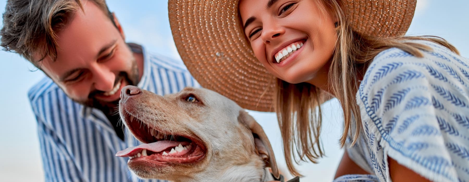 lifestyle image of a couple smiling on a beach with their dog